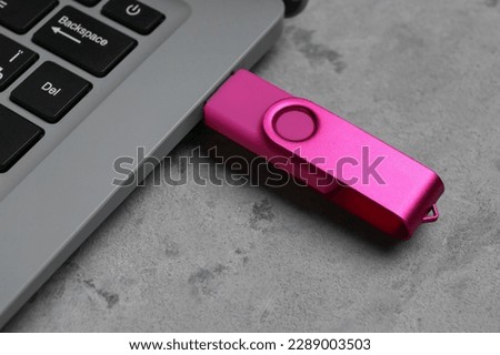 Laptop with pink USB flash drive on grunge background, closeup