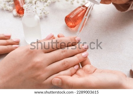 Manicure master applying cuticle oil onto female fingernails on light background, closeup Royalty-Free Stock Photo #2289003615
