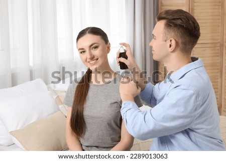 Man spraying medication into woman's ear at home