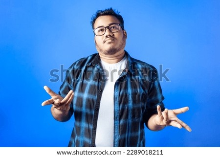 indian man with a shrugging facial expression confused in blue backdrop