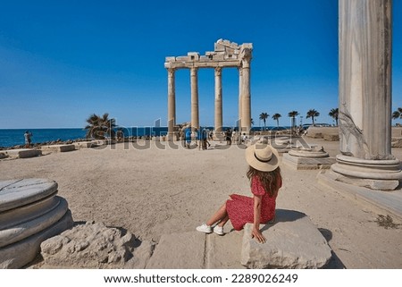 Young tourist girl with hat and red dress is posing in front of the temple of Apollon, ancient city of Side, Manavgat, Antalya, Turkey Royalty-Free Stock Photo #2289026249