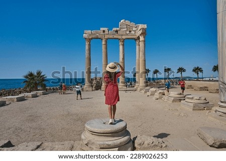 Young tourist girl with hat and red dress is posing in front of the temple of Apollon, ancient city of Side, Manavgat, Antalya, Turkey Royalty-Free Stock Photo #2289026253