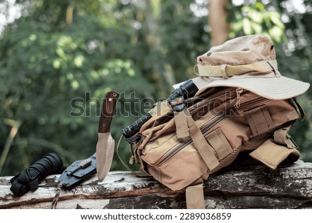 Equipment for survival bucket hat backpack hiking knife camping flashlight resting on wooden timber in the background is a jungle Royalty-Free Stock Photo #2289036859