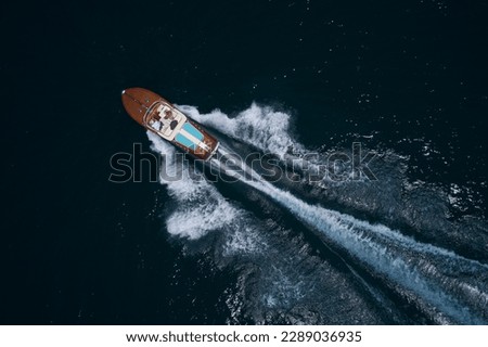 Luxurious wooden boat with people moving fast on dark water top view. Classic Italian wooden boat fast moving aerial view. Top view of a wooden powerful motor boat. Royalty-Free Stock Photo #2289036935