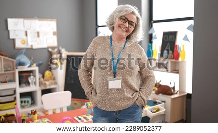 Middle age woman with grey hair preschool teacher smiling confident standing at kindergarten Royalty-Free Stock Photo #2289052377