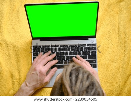 Guy Uses Green Screen notebook. Young man lying on yellow blanket on the bed and uses laptop to work or browse Internet online, typing text on keyboard, top view. Copy space for advertising or design.