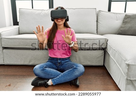 Young latin woman playing video game using vr goggles at home