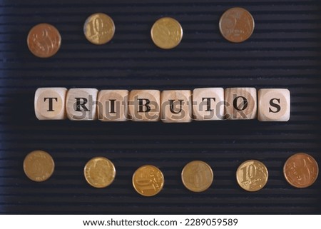 The word tributes in Brazilian Portuguese written on wooden dice with coins from Brazil in the composition. Black background.
 Royalty-Free Stock Photo #2289059589