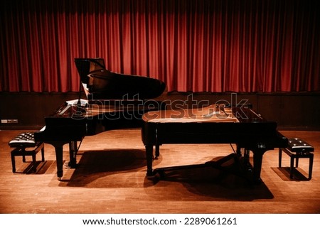 Two grand pianos in the concert hall with red curtains.