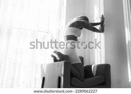 a slender blonde on a chair by the window demonstrates stretching and plastic surgery