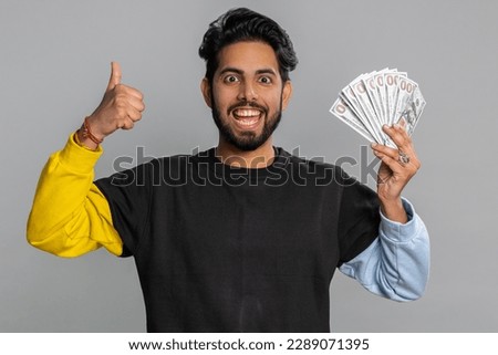 Rich pleased boss hindu man waving money dollar cash banknotes bills like a fan, success business career, lottery winner, big income, wealth. Handsome indian guy isolated on gray background, indoor