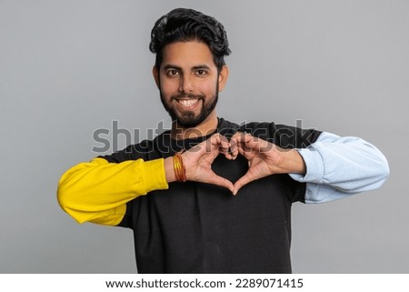 Man in love. Smiling bearded indian man 25 years old makes heart gesture demonstrates love sign expresses good feelings and sympathy. Handsome hindu young guy isolated alone on gray studio background