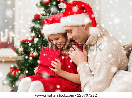 christmas, holidays, family and people concept - smiling father and daughter in santa hats holding gift box at home