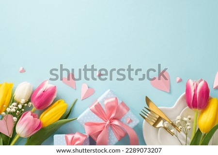 Mother's day concept. Top view flat lay of trendy table setting featuring plates, cutlery, tulips, gift boxes and decorative hearts on pastel blue background. Empty space for text or advert Royalty-Free Stock Photo #2289073207