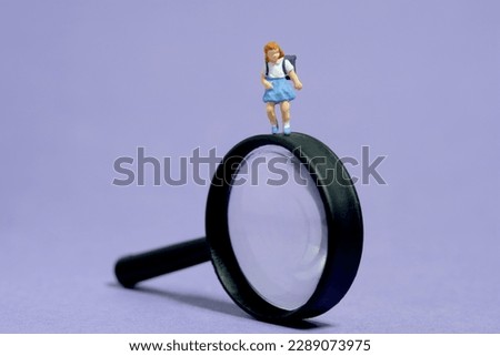 Miniature people toy figure photography. Children curiosity concept. A girl kindergarten student standing above black magnifier glass. Isolated on purple background. Image photo