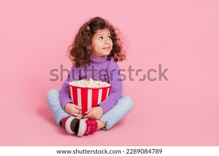 Full length photo of cheerful dreamy small kid wear violet sweater eating pop corn looking empty space isolated pink color background
