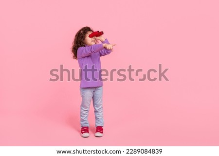 Full length photo of excited little child dressed purple pullover watching binoculars pointing empty space isolated pink color background