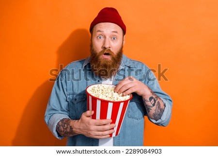 Photo of young funny excited emotion surprised eating popcorn watching comedy good mood vacation rest time isolated on orange color background