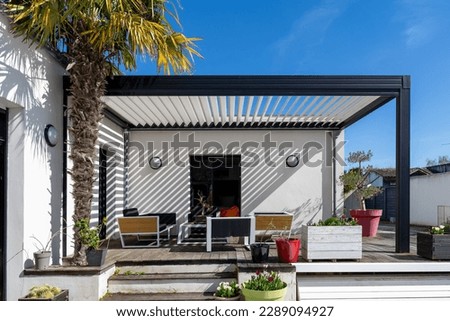 Trendy outdoor patio pergola shade structure, awning and patio roof, garden lounge, chairs, metal grill surrounded by landscaping Royalty-Free Stock Photo #2289094927