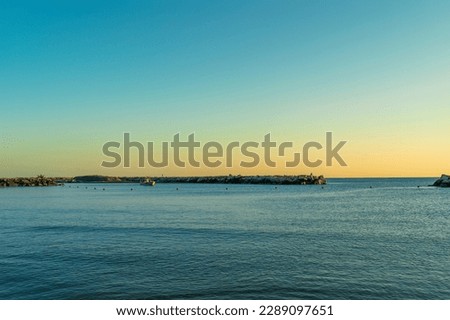 Sea bay protected by a stone pier in the early morning at dawn, a fishing boat sails on the sea against the backdrop of beautiful nature, authentic sustainable development in unity with nature