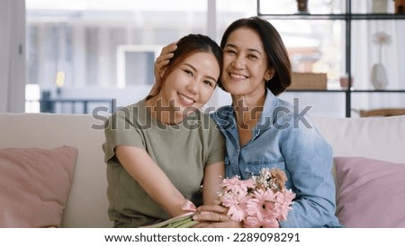 Happy time Mother day grown up child girl looking at camera cuddle hug give flower bouquet gift to mature mum. Love kiss care mom asia middle age adult people smile enjoy relax sitting at home sofa.