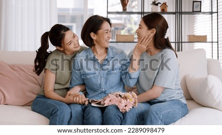 Happy time May Mother day cuddle hug care love face to face kiss cheek to mature mum. Asia middle aged old mom adult people smile enjoy receive gift flower from young child sitting at home sofa relax. Royalty-Free Stock Photo #2289098479