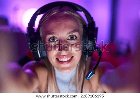 Young blonde woman streamer smiling confident make selfie by camera at gaming room