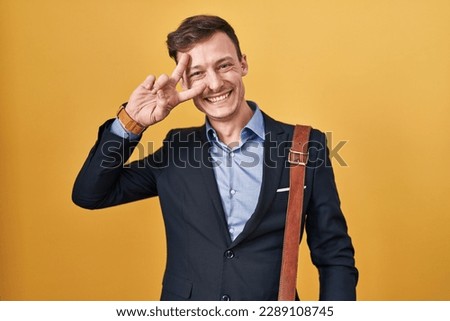 Caucasian business man over yellow background doing peace symbol with fingers over face, smiling cheerful showing victory 