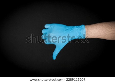 Thumb down shown by a hand in blue gloves.