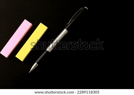 This stock photo features a black table as the background, with yellow and pink sticky notes and a black pen placed on top. The composition is minimalist and perfect for illustrating creativity.