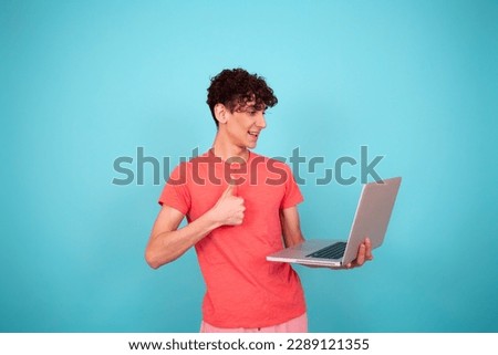 A young student in a pink t-shirt with a laptop in his hands is preparing a report. Blue background.