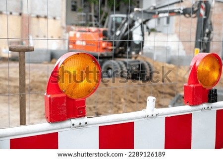 Close-up detail view orange flasher safety blinker light barrier against fence construction site work area. Security equipmnent barricade fuse lamp city street building construction machinery traffic