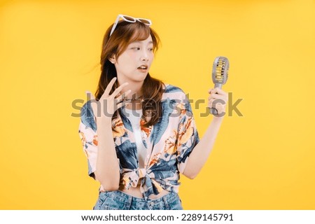 Young Asian woman using a portable fan on yellow background