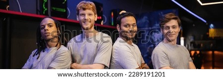 Positive interracial gamers looking at camera and posing in cyber club, banner