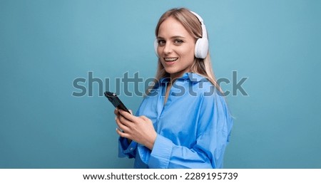 close-up of an attractive girl in wireless large headphones who knows how to relax with music on a blue background