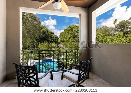 Backyard of elegant and luxurious mansion, with palms and lots of plants around, beautiful covered patio pool, outdoor furniture, shortgrass, basketball court and blue sky with clouds