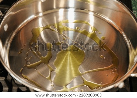 View of a stainless steel frying pan with olive oil heating up on top of a stove.