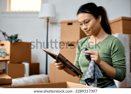 Young Asian woman cleaning photo frame while unpacking her belongings and moving in a new home.
