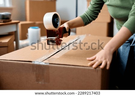 Close up of woman taping carboard boxes while relocating into a new home. Royalty-Free Stock Photo #2289217403