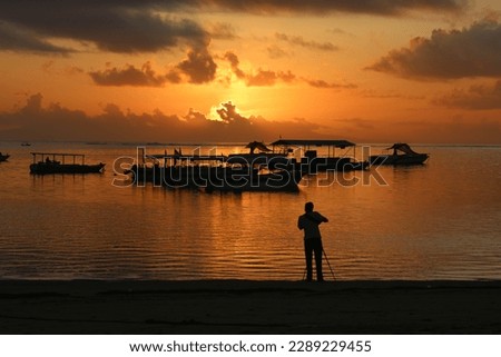Silhouette of photographer take picture of a stunning sunset in Tanjung Benoa Beach Bali. Calm sea, silhouette of a fishing boat, Nature Background.