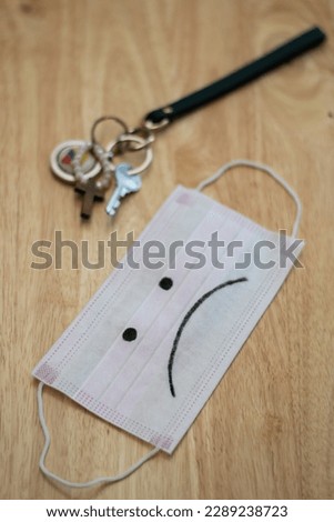 Vertical view of a mask with a sad face drawn and a house key over a table of wood