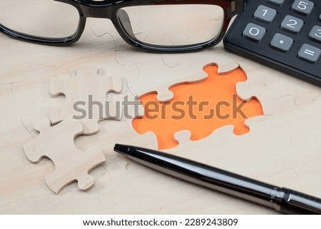 Missing puzzles with orange color opening. A pen, calculator and eyeglasses at the side. Copy space for text