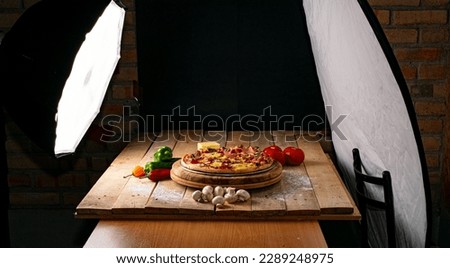 Pizza being photographed in a studio, on a wooden table and dark background