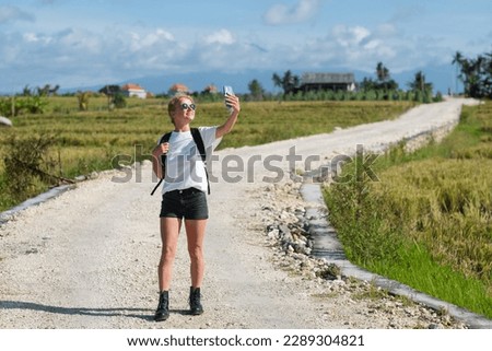 A young blogger girl walks along the road and takes a selfie on the phone, against the background of the silhouette of mountains.