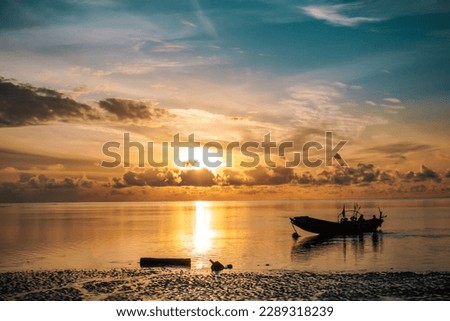 The golden sun rises over the Andaman Sea, casting a warm glow over the tranquil water. A parked boat bobs gently on the ocean, ready for a day of adventure in paradise Royalty-Free Stock Photo #2289318239