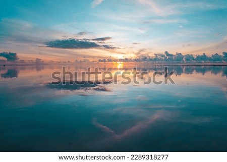 The tranquil sea is a picture of perfection on an early morning, with a stunning blue and orange sky reflected flawlessly in the still water. Not a single wave disturbs the serene scene