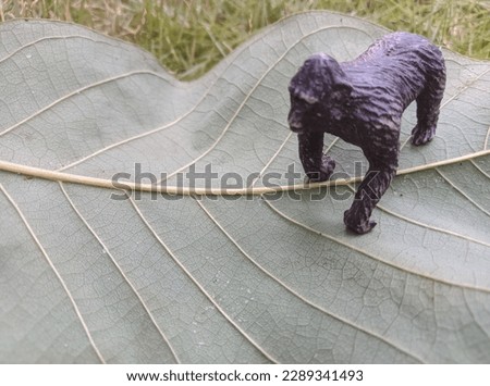A black plastic toy gorilla on an upturned leaf near the grass.