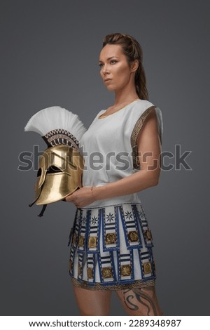 Studio shot of female greek warrior dressed in light armor and holding golden helmet.