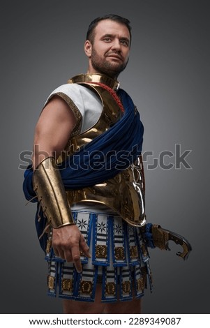 Studio shot of handsome greek warlord holding golden helmet against grey background.