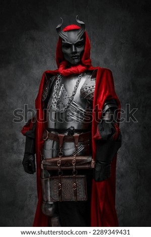 Shot of leader of esoteric cult dressed in silver armor and red mantle with horned mask. Royalty-Free Stock Photo #2289349431
